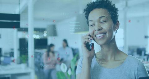 Smiling woman talking on smartphone in modern open office with colleagues and plants