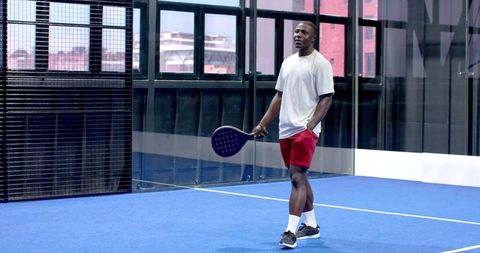 Man relaxing on blue padel court holding racket, modern sports facility