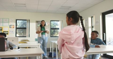 Teacher leading tablet lesson while student in pink hoodie standing in modern classroom
