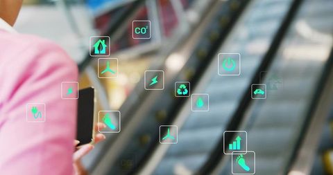 Businesswoman holding smartphone near escalator displaying green sustainability energy icons