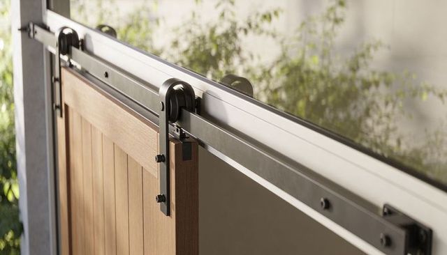 Modern sliding wooden barn door with matte-black top-rail rollers at sunlit patio entry