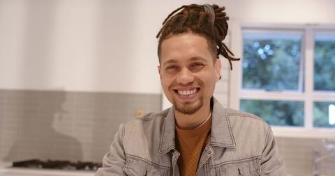 Smiling african american man leaning on kitchen counter in modern home wearing denim jacket