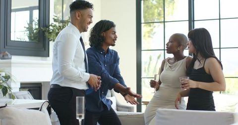 Networking and chatting at cocktail party in sunlit modern living room with champagne flutes