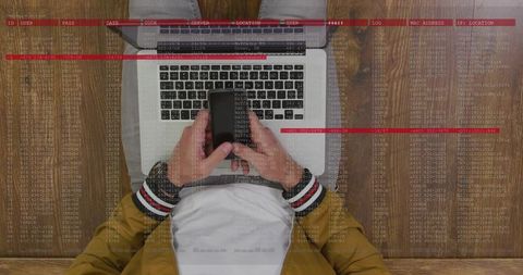 Overhead laptop and smartphone showing code overlay and red alerts for cybersecurity