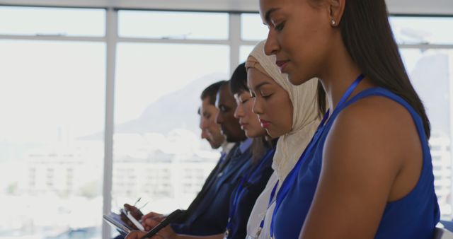 Diverse group of business professionals attending a corporate presentation in an office. They are focused and attentive. Ideal for depicting corporate training, teamwork, diversity in workplace, professional development, and business seminars.