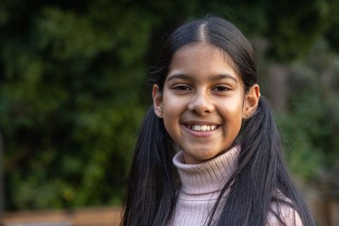 Smiling indian girl wearing pale pink turtleneck outdoors closeup portrait with pigtails