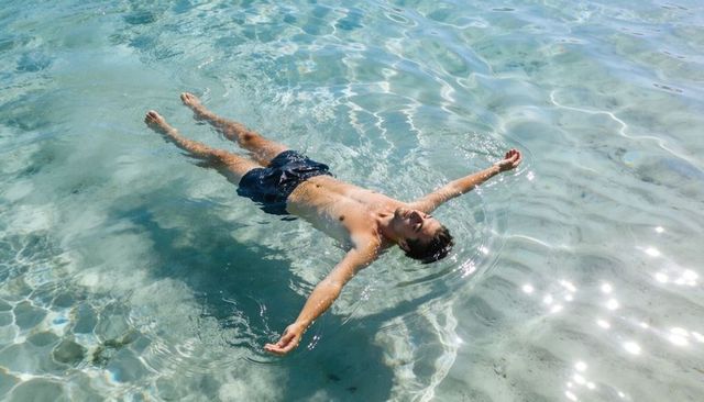 Adult man floating on turquoise water, relaxing on back in shallow sunlit lagoon