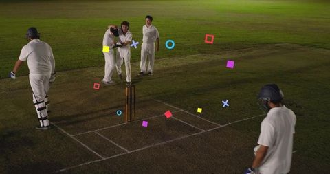 Night cricket team celebrating wicket hugging near stumps on grass pitch under lights