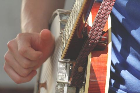 Close-up of hand playing a banjo with brown strap