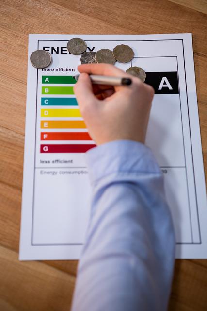 Woman writing on energy efficiency rating chart on a wooden table