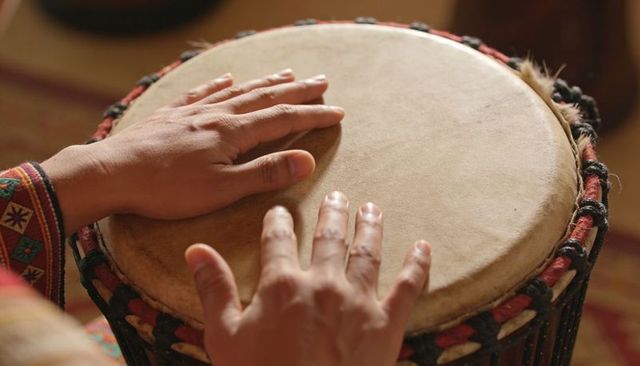 Closeup hands playing djembe drum with colorful sleeve and rope-tuned skin