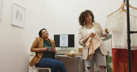 Diverse fashion designers collaborating in studio, examining blouse and garment sketches