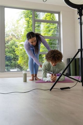 African american trainer guiding trainee doing plank core workout in bright home studio