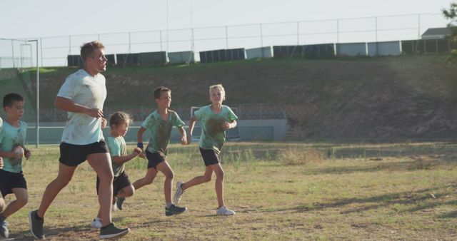 Happy caucasian male instructor and children running across bootcamp training course. Fitness, childhood, friendship, challenge and healthy lifestyle.