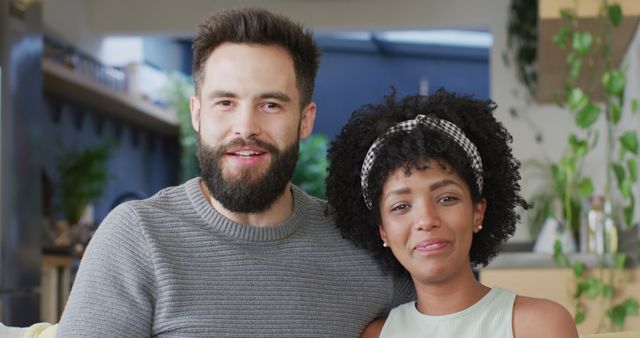 This image of a smiling mixed-race couple relaxing at home can be used in articles or advertisements focused on relationships, family life, inclusivity, or domestic happiness. It is perfect for content promoting togetherness, love, and positive relationships.