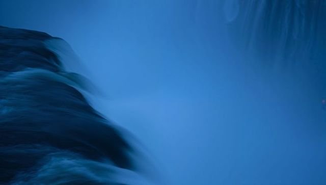 Flowing long-exposure waterfall creating smooth mist over river gorge at dusk