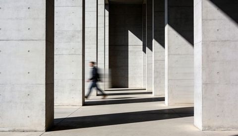 Blurred man walking through concrete colonnade with strong diagonal shadows and geometry