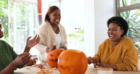 Laughing friends carving jack-o'-lanterns at sunlit table cozy autumn pumpkin crafting