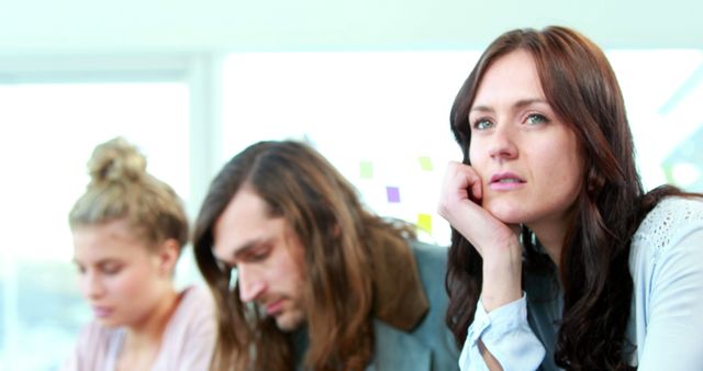 Young adults sitting together in a casual office setting, listening intently. Could represent business collaboration, teamwork, brainstorming sessions, or educational settings. Use for themes involving concentration, group activities, and professional environments.