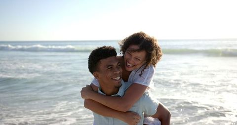 Happy couple enjoying romantic piggyback on sunny beach