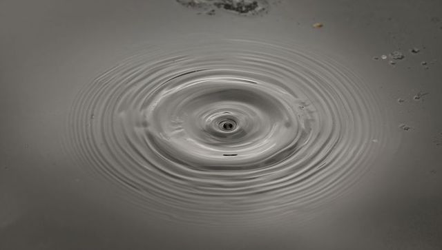 Monochrome water ripple forming central micro-whirlpool with concentric ripple rings