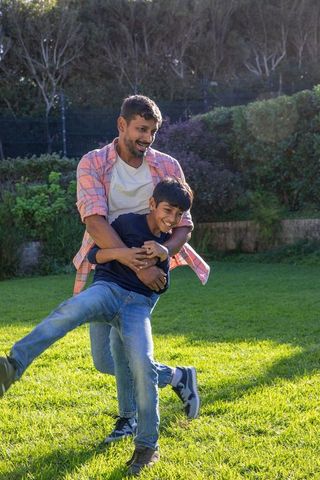 Father and son playing laughing outdoor in sunny backyard garden