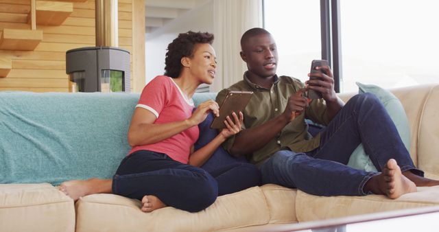 A couple sitting on a sofa at home, engaging with their smartphones. This can be used in promotions for family lifestyle, home relaxation, or technology-related services. It showcases modern living, technology use at home, and the joy of shared moments. Perfect for social media campaigns, blogs about home life, and advertisements for digital products.