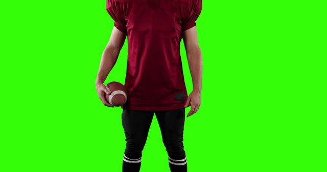 Football player in red jersey holding ball against green screen background. Ideal for graphic design, video production, advertisements, and sports-related projects where custom backgrounds or special effects are required.