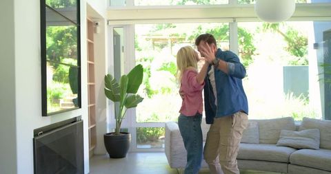 Couple dancing playfully in bright modern living room with glass doors and garden view