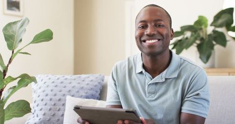 Smiling Man Using Tablet on Sofa in Modern Living Room