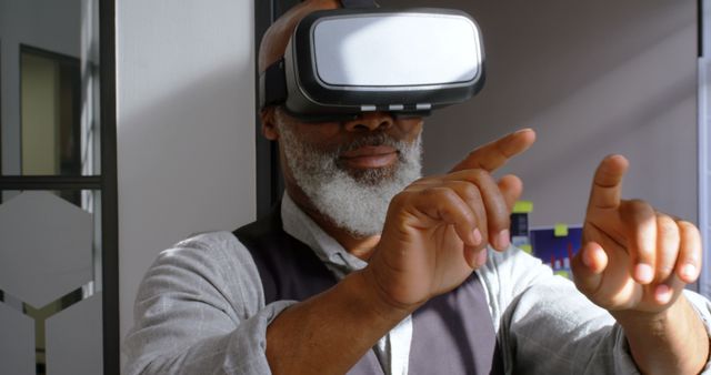 An older man with a beard is using a virtual reality headset, intently engaging with the digital environment. This image can be used for illustrating technology adoption among the elderly, virtual reality applications, innovation in tech, or user experience tutorials.