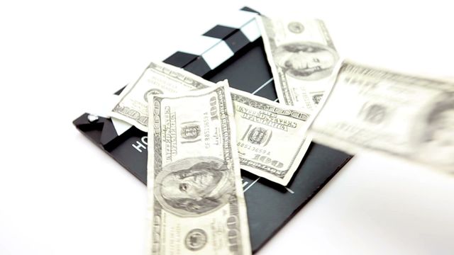 US dollar bills scattered on a director's clapboard, symbolizing investment in the film industry. Useful for topics on financing films, budgeting, cinematography, and symbolic representation of cinema as a business enterprise.