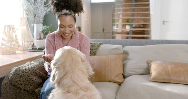 Happy biracial woman petting golden retriever dog at home, copy space. Lifestyle, animal and domestic life, unaltered.