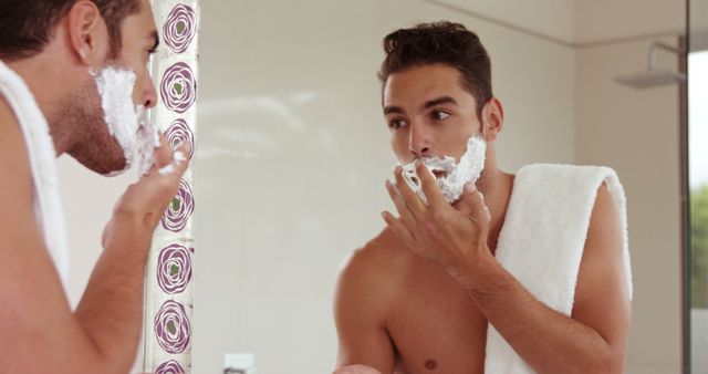 Young man shaving and checking his reflection in bathroom mirror - Download Free Stock Images Pikwizard.com