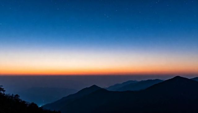 Layered mountain ridges at twilight with starry sky and warm horizon glow panorama