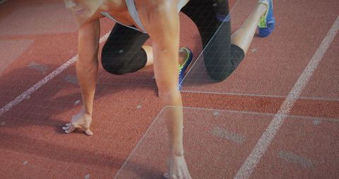 Woman sprinter preparing at starting line on red track wearing capris and blue shoes
