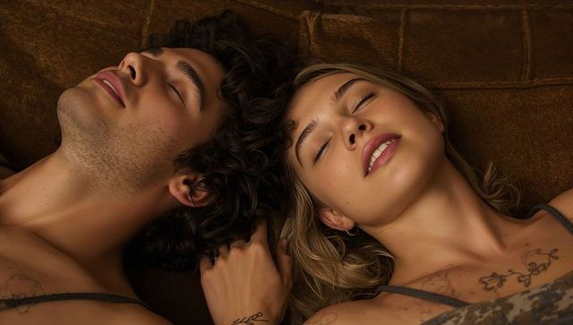 Young couple reclining together on brown sofa showing tattoos, relaxed intimacy, cozy warmth