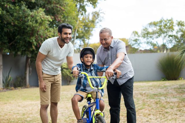 Father and grandfather assisting boy for riding bicycle while standing in yard