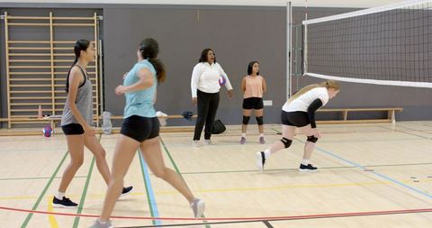 Female volleyball team practicing drills with coach on indoor school gym court and warm-up