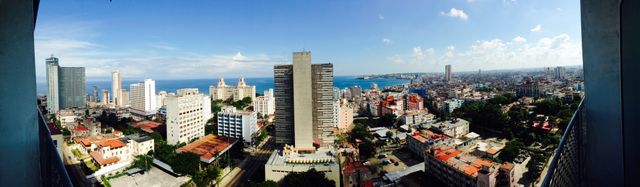 Wide view of Havana, showing both modern and historical buildings under a clear blue sky, perfect for travel blogs, urban studies, tourism promotions, and cultural presentations. Highlights the vibrant mix of architecture against a coastal backdrop.