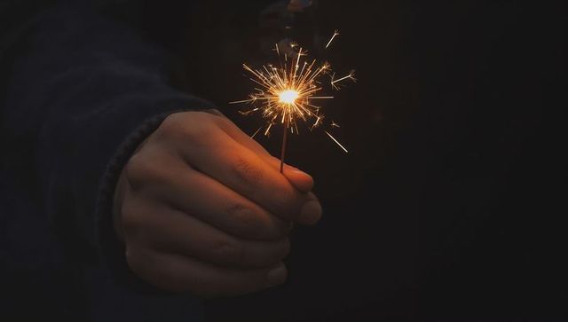 Closeup Hand Holding Lit Sparkler Against Dark Background Celebrating Nighttime Warmth