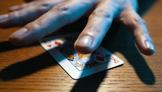 Placing hand splaying three fingers over king of diamonds on wooden table, blue light