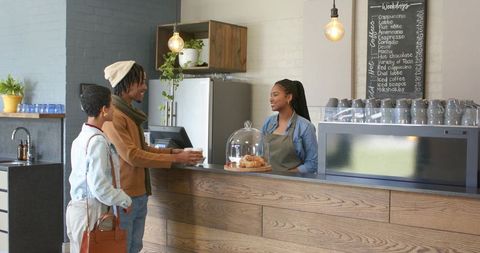 Couple ordering coffee at modern cafe counter with friendly barista and pastries