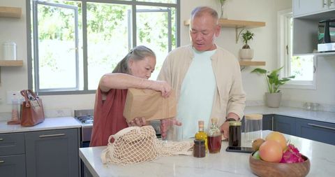 Senior couple unpacking groceries at kitchen island using reusable mesh bag and glass jars