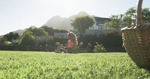 Little girl wearing bunny ears enjoying backyard picnic on sunlit lawn