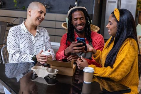 Multicultural friends laughing and sharing smartphone over coffee in cozy modern cafe