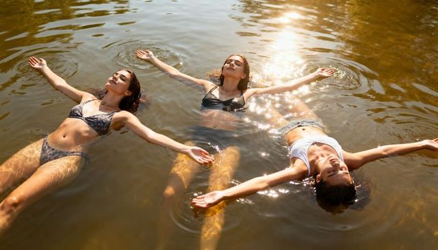 Three women floating and relaxing on sunlit lake water with shimmering reflections