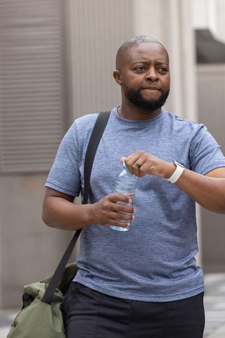 Male commuter opening water bottle while carrying duffel bag on city sidewalk