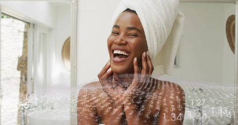 Laughing woman wearing towel turban at bathroom vanity with digital data overlay