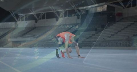 Sprinter with carbon running blade bracing for start on indoor blue track in empty stadium